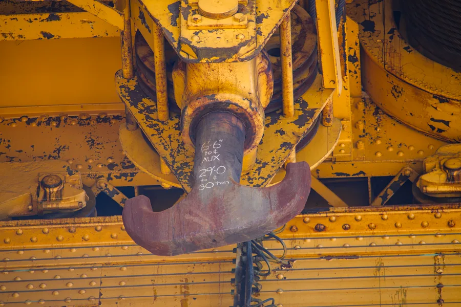 Yellow crane with writing on the hook in a dry dock at the Philadelphia Shipyard.